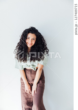 Curly brunette woman in clothes smiling on white background 127489715