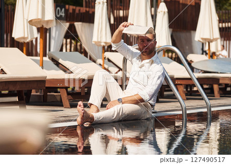 Sitting, taking a rest. Handsome man in formal clothes is in the pool 127490517