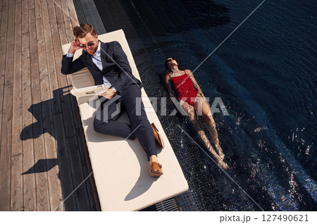 Reading the newspaper. Man with woman is in the pool together Reading the newspaper. Man with woman is in the pool together 127490621