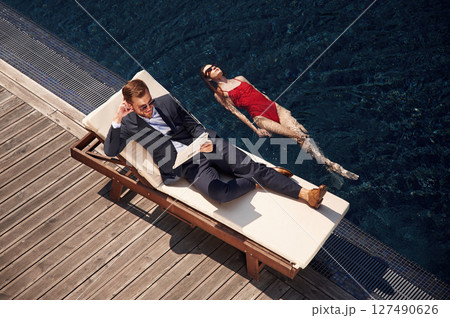 Business clothes, reading newspaper. Man with woman is in the pool together Business clothes, reading newspaper. Man with woman is in the pool together 127490626