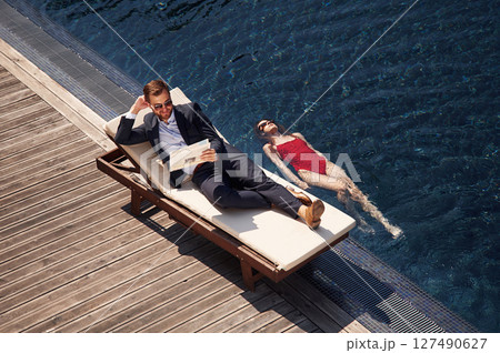 Business clothes, reading newspaper. Man with woman is in the pool together Business clothes, reading newspaper. Man with woman is in the pool together 127490627