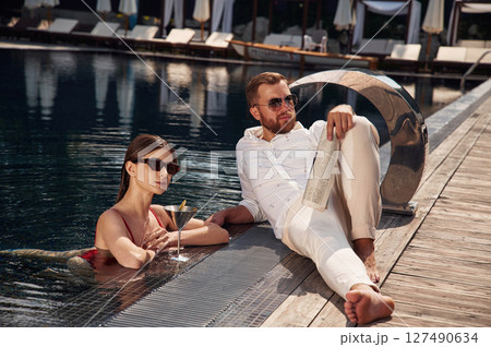 With newspaper in hand. Man with woman is in the pool together With newspaper in hand. Man with woman is in the pool together 127490634