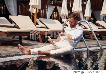 Holding newspaper. Handsome man in formal clothes is in the pool Holding newspaper. Handsome man in formal clothes is in the pool 127490796