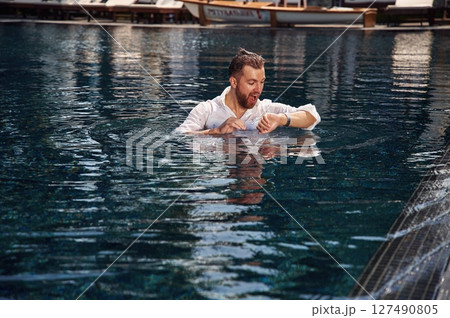Checking the time, in the water. Handsome man in formal clothes is in the pool Checking the time, in the water. Handsome man in formal clothes is in the pool 127490805