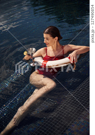 With drink in hand. Young woman in red swimsuit is in the pool With drink in hand. Young woman in red swimsuit is in the pool 127490854