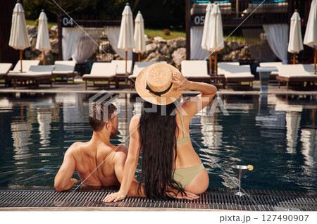 Rear view. Man with woman is in the pool together Rear view. Man with woman is in the pool together 127490907