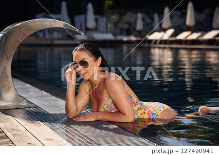 Standing, leaning on the surface. Beautiful woman that is in swimsuit is in the pool 127490941