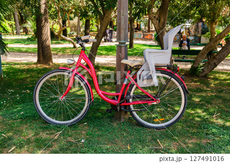 Parked red bicycle with child seat. Family lifestyle, eco-friendly transport, and urban leisure in green outdoor spaces. 127491016