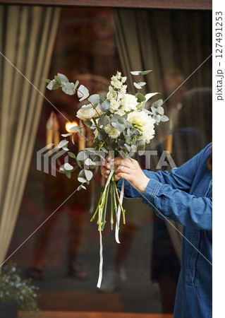 Against the window. Close up view of woman that is with flowers in hands Against the window. Close up view of woman that is with flowers in hands 127491253
