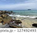 Rocky Tropical Beach with Clear Waves and Distant Island  127492493
