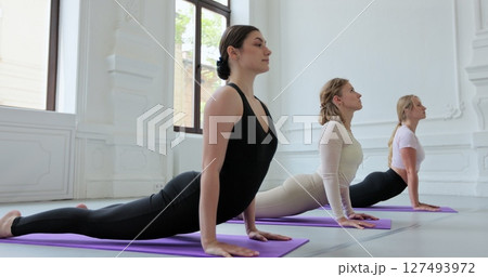 Group of four young women are practicing yoga on mats in a large, bright room. Concept of healthy lifestyles and self development. 127493972