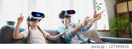Father and daughter enjoying virtual reality headset experience in cozy living room setting 127494028