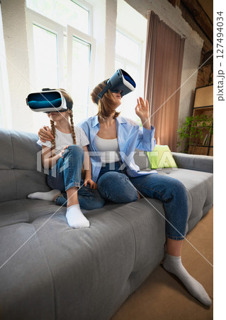Mother and daughter bonding through virtual reality technology experience in cozy living room Mother and daughter bonding through virtual reality technology experience in cozy living room 127494034