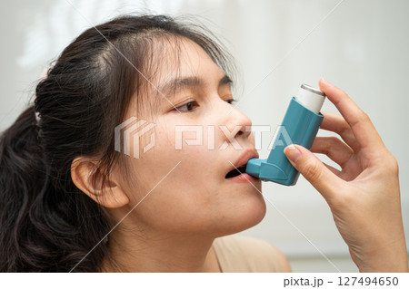 Asthma and chronic obstructive pulmonary disease COPD, Asian woman using metered dose inhaler MDI. 127494650