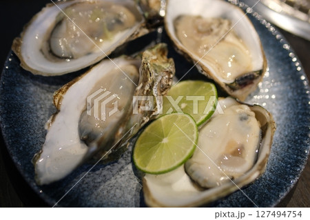 Oysters on a dish with ice, with lemon, lime, and white wine, overhead flat lay shot on a black slate background 127494754