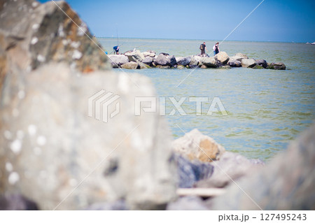 Numerous People Strolling on Large Rocks Near the Water Under a Beautiful Bright Blue Sky 127495243