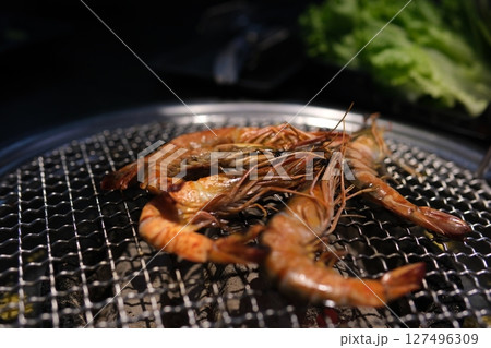Grilled skewer shrimps and fresh vegetables served on black stony plate on wooden table 127496309