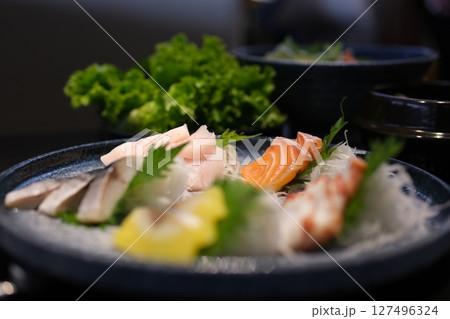 Delicate slices of fresh salmon sashimi are artfully arranged on an elegant plate, garnished with herbs and edible flowers, embodying fine dining. 127496324