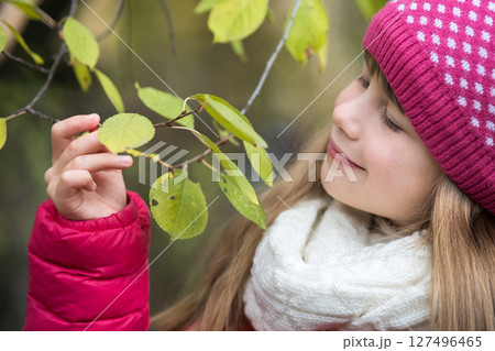 Pretty child girl wearing warm winter clothes holding tree branch with green leaves in cold weather outdoors. 127496465