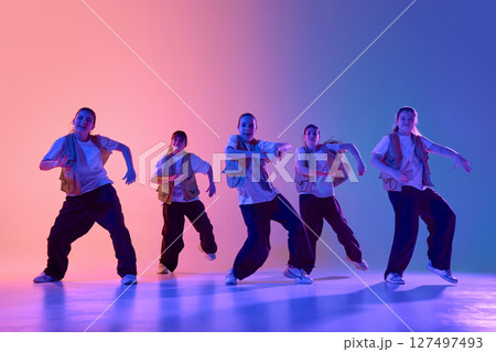 Energetic dance group performing under vibrant colorful lighting in urban dance studio 127497493