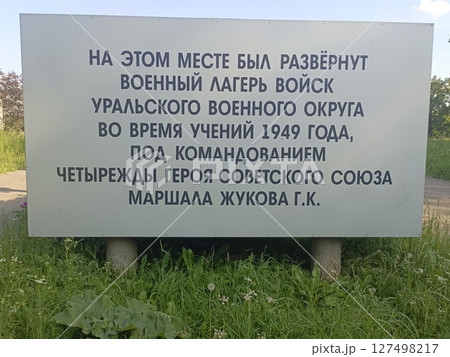 A military camp sign in Russian, detailing the history of the Ural Military District during exercises in 1949 under General Zhukov's command. Surrounded by grass. A military camp sign in Russian, detailing the history of the Ural Military District during exercises in 1949 under General Zhukov's command. Surrounded by grass. 127498217