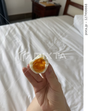 a bitten egg with a hard-boiled bright orange yolk in the hands of a girl against the background of a bed a bitten egg with a hard-boiled bright orange yolk in the hands of a girl against the background of a bed 127498668