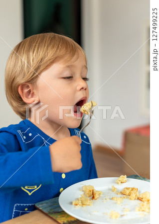A child wearing a blue shirt is sitting at a table and eating enthusiastically. The moment captures a sense of appetite and the carefree nature of childhood. Diet for kids, homemade food A child wearing a blue shirt is sitting at a table and eating enthusiastically. The moment captures a sense of appetite and the carefree nature of childhood. Diet for kids, homemade food 127499225