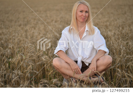 Woman meditating while sitting cross-legged in a golden wheat field during sunset hours for a sense of peace and tranquility 127499255