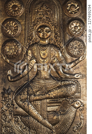Brass relief sculpture featuring an intricately detailed depiction of a seated deity 127499294