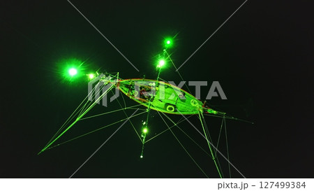 Aerial night view of a traditional Thai squid fishing boat using green lights to attract its prey in the waters surrounding Koh Phangan, Thailand, showcasing a unique fishing technique 127499384