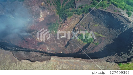 Volcanic fumes are rising from inside the crater of Mount Kelimutu in Flores, Indonesia, surrounded by lush vegetation, showing the raw power of nature 127499395