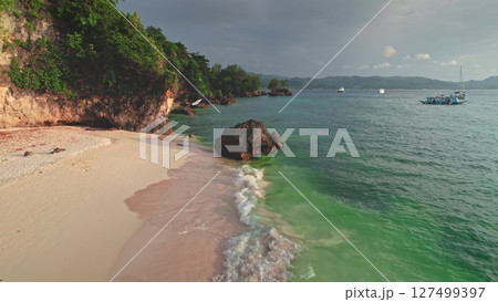 Crystal-clear turquoise water gently washes the pristine white sand of Cagban Beach, Boracay Island, Philippines, while boats dot the horizon under a cloudy sky 127499397