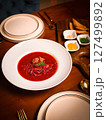 Traditional Ukrainian borscht with beef and dill served in a white bowl, styled with condiments and pastry on a warm wooden restaurant table 127499892