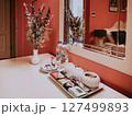 Boutique hotel interior with mirror, flowers, and tray of tea, snacks, and bottled water styled on a clean vanity in a soft coral-colored guest room 127499893
