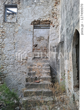 Ruins of a medieval house in Alicante reveal crumbling stone steps leading to a weathered doorway. Nature reclaims the structure, highlighting its eerie and abandoned atmosphere. 127499970