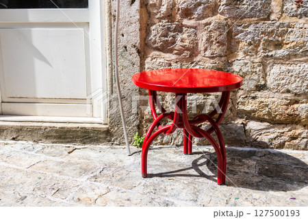 Bright red stool beside stone wall. Street furniture, color contrast, and outdoor simplicity. 127500193