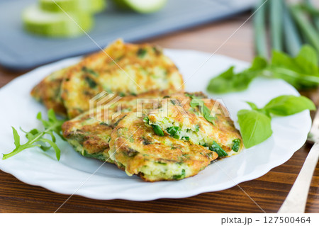 fried zucchini fritters with green onions in a plate on a wooden table 127500464