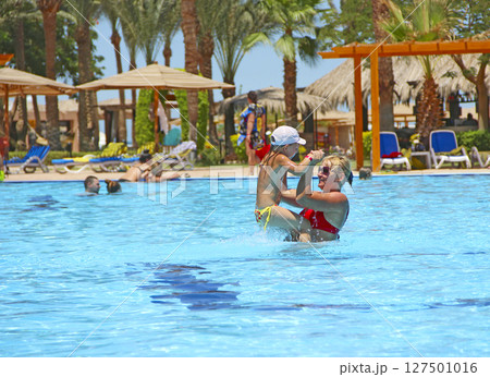 Mother catching her daughter jumping into swimming pool. Happy holidays Mother catching her daughter jumping into swimming pool. Happy holidays 127501016
