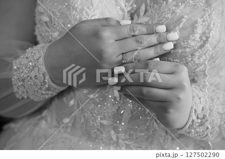 Elegant Wedding Ring Close-Up: Bride's Hands Displaying Diamond Band on Lace Dress, Black and White Photography. 127502290