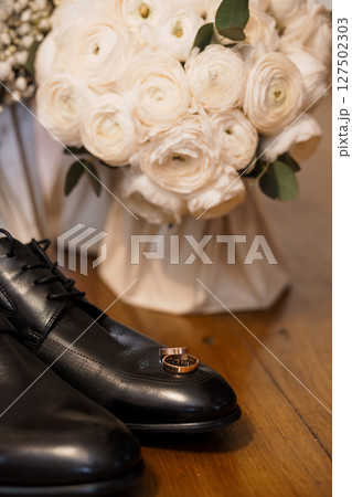 Wedding Day Details Still Life: Black Leather Shoes, Gold Rings, White Ranunculus Bouquet, Dark Wood Surface, Elegant Romantic Style Wedding Day Details Still Life: Black Leather Shoes, Gold Rings, White Ranunculus Bouquet, Dark Wood Surface, Elegant Romantic Style 127502303