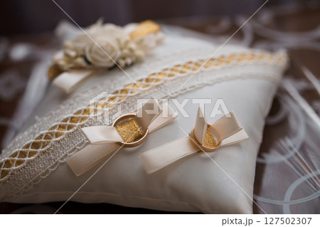Elegant Wedding Ring Pillow with Gold Bands and Lace Trim: White Satin Cushion with Floral Accent for Nuptial Ceremony Elegant Wedding Ring Pillow with Gold Bands and Lace Trim: White Satin Cushion with Floral Accent for Nuptial Ceremony 127502307