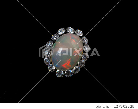 Exquisite Oval Opal Ring with Sparkling Diamond Halo. Luxury Fine Jewelry, Black Background, Gemstone Close-up, Colorful Fire, Elegant Design Exquisite Oval Opal Ring with Sparkling Diamond Halo. Luxury Fine Jewelry, Black Background, Gemstone Close-up, Colorful Fire, Elegant Design 127502329