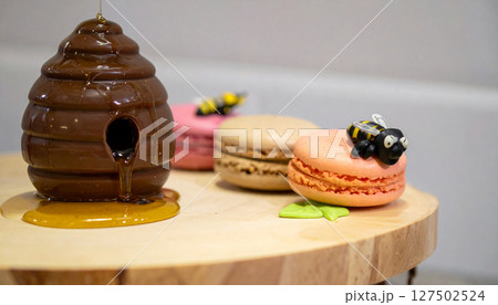 Chocolate covered beehive dripping honey onto macaron flowers. Generated Image 127502524