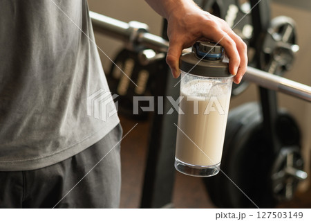 Close up of man hand with protein shaker at gym. Fitness healthy lifestyle concept. Supplement product, creatine, glutamine for workout. Close up of man hand with protein shaker at gym. Fitness healthy lifestyle concept. Supplement product, creatine, glutamine for workout. 127503149