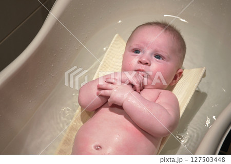 Infant baby boy washed in small bath tub, laying on back, view from above 127503448