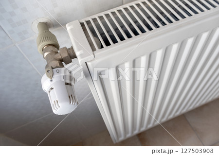 Closeup of heating radiator valve for comfortable temperature regulation on metal radiator on inrerior wall. 127503908