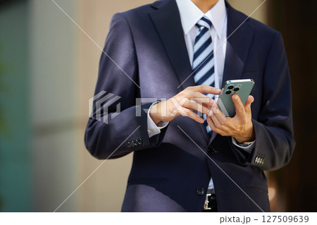 ビジネス街でスマートフォンを見るスーツの若いビジネスマン ビジネス街でスマートフォンを見るスーツの若いビジネスマン 127509639