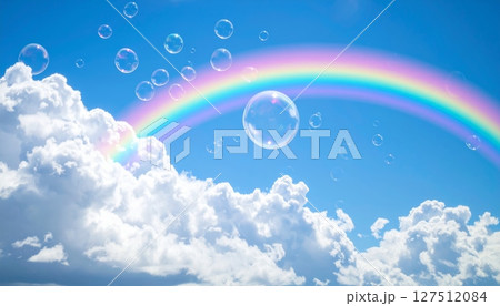 A bright summer day with a vibrant rainbow arching across the blue sky through scattered white clouds 127512084