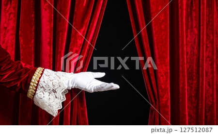 Hand opens the luxurious red velvet curtain on stage, unveiling the highly anticipated show 127512087