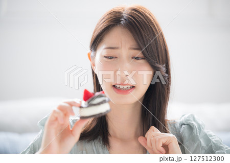 甘いスイーツを食べるか迷う女性　スイーツは別腹だけどダイエットで悩む 127512300